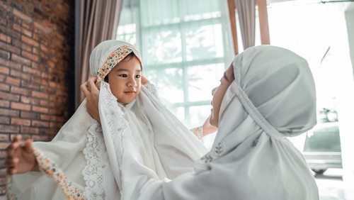 muslim mother help her young daughter to put the scarf on before pray