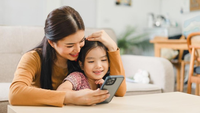 Young mother and daughter enjoying time together with smartphone at home