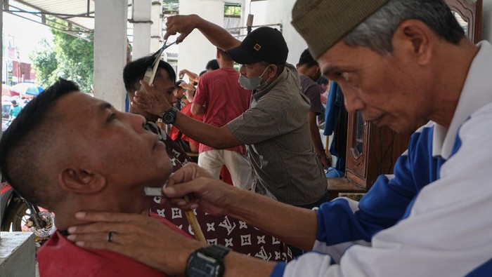 Dua orang tukang pangkas rambut melayani pelanggan di kios cukur rambut di kawasan Korem, Kendari, Sulawesi Tenggara, Kamis (5/6/2025). H-1 menjelang hari raya Idul Adha, jumlah pelanggan yang datang untuk memangkas rambut di kawasan tersebut meningkat sebanyak 100 persen dibandingkan tahun lalu dan hari biasanya dengan tarif Rp30 ribu per orang. ANTARA FOTO/Andry Denisah/bar