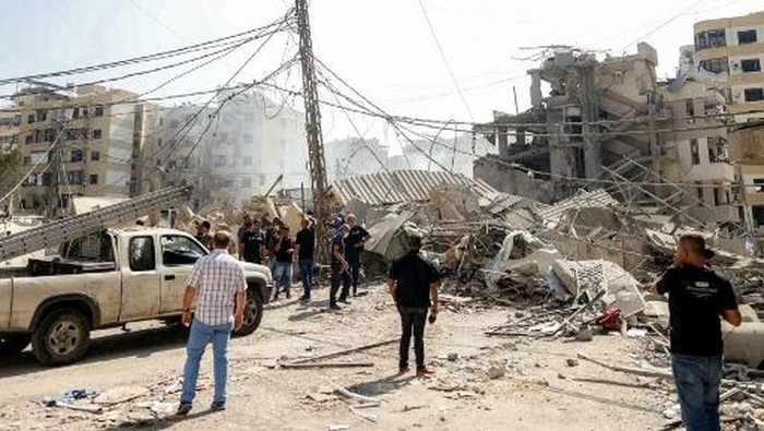 People stand by the rubble of a collapsed building at the site of an overnight Israeli airstrike in the Hadath neighbourhood of Beiruts southern suburbs on June 6, 2025. Israel warned on June 6 that it will keep striking Lebanon until it disarms militant group Hezbollah, hours after it hit south Beirut in what Lebanese leaders called a major ceasefire violation. The attack on what the Israeli military said was Hezbollahs underground drone factories came on the eve of Eid al-Adha, one of the main religious festivals on the Muslim calendar. (Photo by IBRAHIM AMRO / AFP)