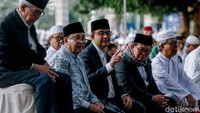 Anies tampak mengenakan peci hitam, kemeja putih, jas hitam dengan sarung bernuansa biru. 