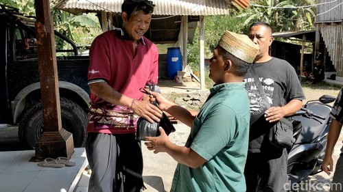 Kepala Kampung Angantiga, M Ramsudin saat memberikan bungkusan daging sapi dan kambing kurban kepada Bendesa Adat Angantiga, Jumat (6/6/2025). (Agus Eka/detikBali)