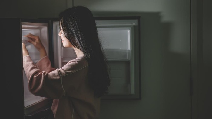 1147888700 an asian chinese female looking for food from the refrigerator during mid night in the kitchen holding a plate
