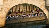 Orang-orang menikmati cuaca yang hangat dan cerah hari musim semi di tepi Sungai Seine dekat jembatan Pont Neuf. Foto: REUTERS/Gonzalo Fuentes