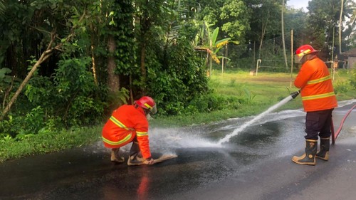 Petugas Damkartan membersihkan ceceran solar dengan menyemprotkan air di Jalan Besang, Desa Ababi, Kecamatan Abang, Karangasem, Minggu (8/6/2025). (Foto: Dok. Damkartan Karangasem)