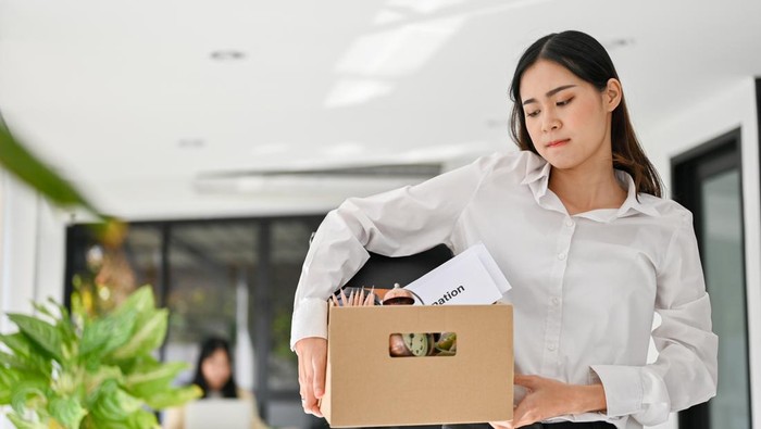Sad and upset young Asian female office worker carrying her belonging, quitting a job, being fired from her boss.