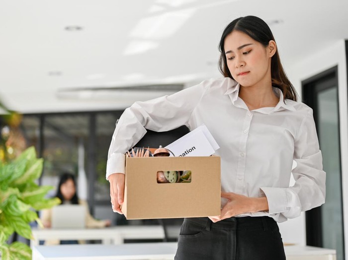 Sad and upset young Asian female office worker carrying her belonging, quitting a job, being fired from her boss.