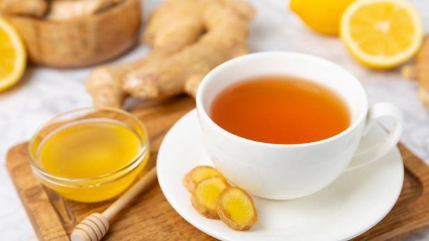 Cup of hot ginger tea with slices of ginger root on wooden background. Warming drink. Alternative medicine. Tea with honey, lemon, ginger and mint. Space for text. Copy space