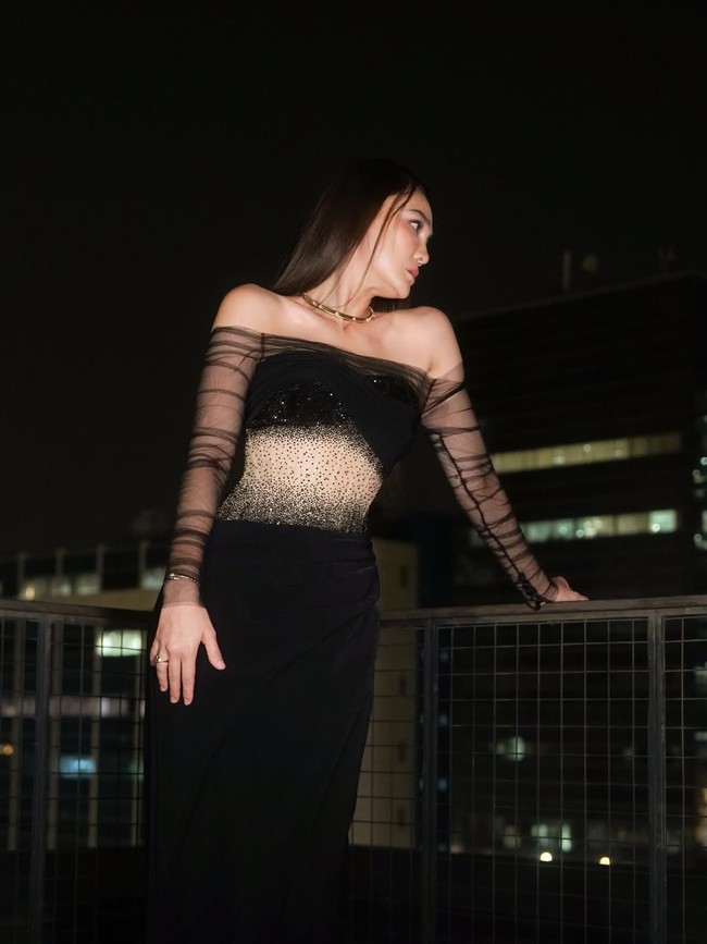 Gaya yang ditampilkan penuh permainan kontras halus. Bagian dada atas dan lengan dibuat dengan bahan hitam transparan, sementara rok bersiluet jam pasir hadir dalam nuansa hitam pekat dengan drapery yang anggun. Foto: Instagram/@hiantjen