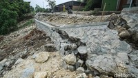 Turap beton yang sebelumnya dibangun sebagai penahan longsor tampak patah dan runtuh.