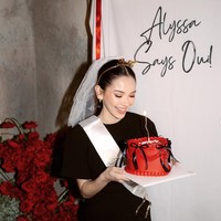 Tak seperti acara bridal shower yang menggunakan kue bergambar jorok, kue bridal shower Alyssa justru tampak simpel dan elegan dengan warna merah dan berhias pita-pita hitam. Dekorasi backdrop di acara tersebut juga tak kalah simpel dengan warna putih dan tulisan Alyssa Says Oui!. Foto: Instagram/@alyssadaguise