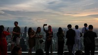 Siluet pengunjung terlihat jelas saat matahari sore mulai turun di balik cakrawala kota Bangkok, menciptakan suasana dramatis di dek observasi. Foto: REUTERS/Athit Perawongmetha