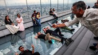 Sejumlah wisatawan berbaring di atas lantai kaca transparan Mahanakhon Skywalk, berfoto sambil merasakan sensasi melayang di atas kota Bangkok dari ketinggian lebih dari 300 meter. Foto: REUTERS/Athit Perawongmetha
