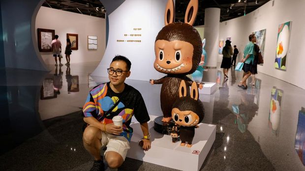 Seorang pria berpose untuk difoto di samping patung Labubu seukuran manusia asli yang dipajang sebelum dilelang di Beijing, Tiongkok, 6 Juni 2025. Patung itu kemudian terjual seharga 820.000 yuan dalam sebuah lelang oleh Yongle International Auction pada hari Selasa. (REUTERS/Tingshu Wang)