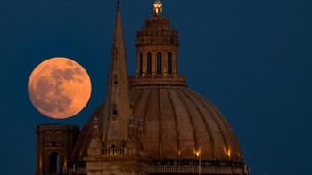 Di Malta, Strawberry Moon terlihat menawan dari kota Sliema, dengan latar menara Katedral St Paul dan kubah Basilica of Our Lady of Mount Carmel di Valletta. Siluet arsitektur kota yang kontras dengan cahaya lembut bulan menciptakan komposisi visual yang dramatis. (REUTERS/Darrin Zammit Lupi)