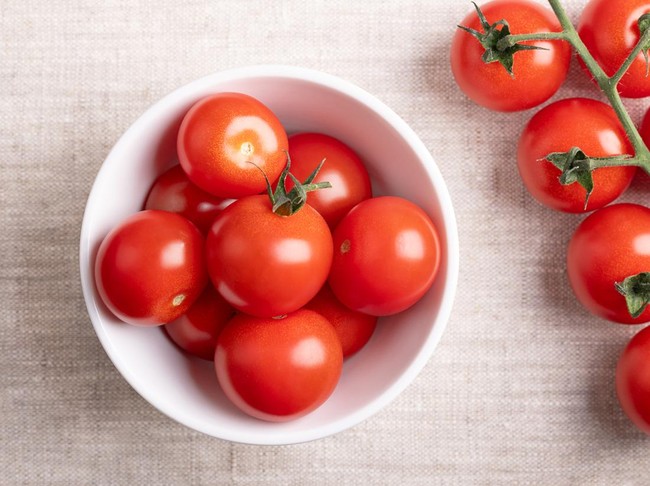 Ilustrasi tomat Red cherry tomatoes in a white bowl on linen fabric. Fresh, ripe type of small and round cocktail tomatoes, on the left side still on the vine, from above. Solanum lycopersicum var. cerasiforme. Photo