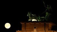 Di Berlin, Jerman, bulan purnama terlihat bersinar di samping patung Quadriga di atas Gerbang Brandenburg. Strawberry Moon sering tampak lebih terang dan lebih besar karena posisinya rendah di cakrawala. (REUTERS/Fabrizio Bensch)  