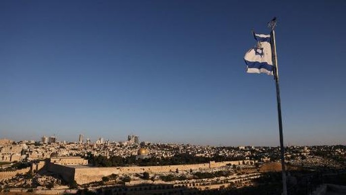 An Israeli flag flutters on the Mount of Olives as the sun rises over Jerusalem and its landmark Dome of the Rock mosque on June 13, 2025, following Israeli Prime Minister Benjamin Netanyahus announcement that a military operation was launched against Iran and would continue for as many days as it takes. Israel carried out strikes targeting nuclear and military sites in Iran early on June 13, after US President Donald Trump warned of a possible massive conflict in the region. (Photo by AHMAD GHARABLI / AFP)