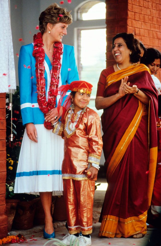 DELHI, INDIA - FEBRUARY 12: Diana, Princess of Wales, wearing a blue and white suit designed by Catherine Walker and a flower garland round her neck, holds hands with a child during a visit to Tamana Special School in New Delhi on February 12, 1992 in Delhi, India. (Photo by Anwar Hussein/Getty Images)