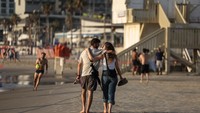 Sepasang kekasih berjalan di pantai Mediterania, di tengah saling serang antara Israel dan Iran, di Tel Aviv, Israel, Senin (16/6/2025). (REUTERS/Ronen Zvulun)  