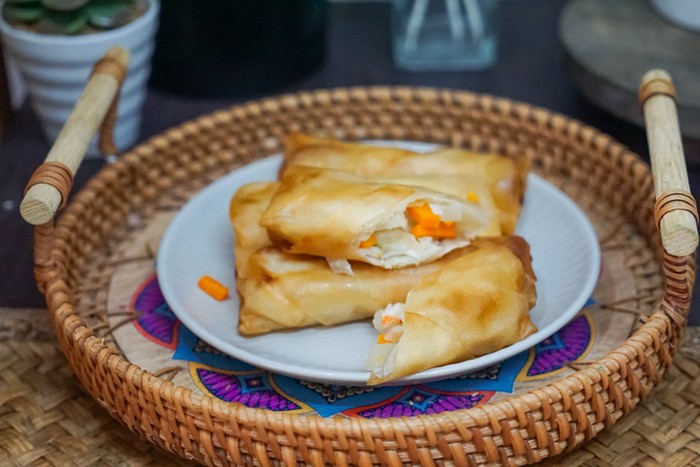 Delicious golden spring rolls displayed in a wicker basket on a plate, filled with fresh vegetables, ideal for culinary presentations, food blogs, menus, and showcasing appetizing cooked treats.