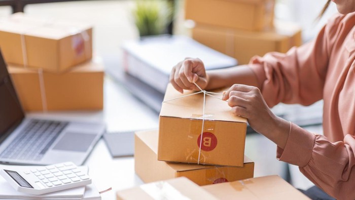 SME Online seller Young Asian woman working on laptop and box checking online order, check goods stock delivery package shipping postal. Asian woman startup SME small business at home office