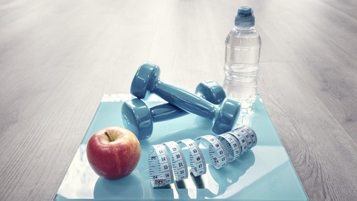 Fitness dumbbells, bathroom scales, apple and tape measure in gym, diet concept
