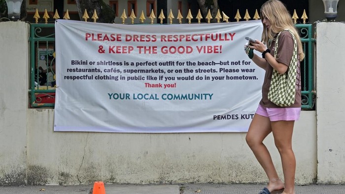 Pakai Bikini Bisa Kena Tegur, Ini Aturan Baru di Kuta NTB Wisatawan asing melintas di depan spanduk terkait penggunaan pakaian bikini di Kuta, Kecamatan Pujut, Praya, Lombok Tengah, NTB, Jumat (20/6/2025). Pemerintah Desa (Pemdes) Kuta mengeluarkan imbauan atau peringatan kepada wisatawan baik domestik maupun mancanegara yang datang berwisata di kawasan wisata Kuta untuk tidak memakai bikini atau berpakaian minim saat berada di area publik seperti pasar, restoran, area perkampungan hingga jalan umum. ANTARA FOTO/Ahmad Subaidi/agr