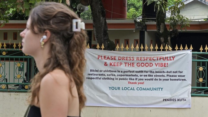 Wisatawan asing melintas di depan spanduk terkait penggunaan pakaian bikini di Kuta, Kecamatan Pujut, Praya, Lombok Tengah, NTB, Jumat (20/6/2025). Pemerintah Desa (Pemdes) Kuta mengeluarkan imbauan atau peringatan kepada wisatawan baik domestik maupun mancanegara yang datang berwisata di kawasan wisata Kuta untuk tidak memakai bikini atau berpakaian minim saat berada di area publik seperti pasar, restoran, area perkampungan hingga jalan umum. ANTARA FOTO/Ahmad Subaidi/agr