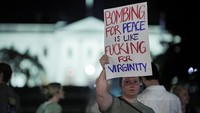Pendemo juga mengecam klaim Trump bahwa serangan ini demi perdamaian. Dengan tajam mereka mencibir argumen militer dengan poster provokatif: “bombing for peace is like fucking for virginity”, mengkritik bahwa kekerasan tidak pernah menghasilkan hasil yang sahih dan abadi. (REUTERS/Ken Cedeno)