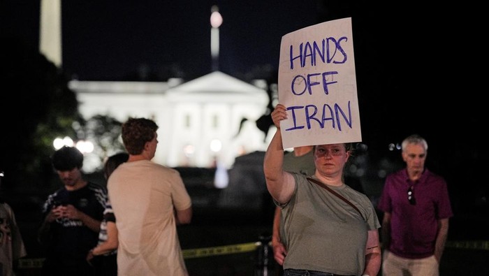 Warga AS Marah Trump Ikutan Perangi Iran Emma Edwards holds a poster while protesting outside Lafayette Park, following U.S. strikes on Iran's nuclear facilities, in Washington, D.C., U.S., June 21, 2025. REUTERS/Ken Cedeno