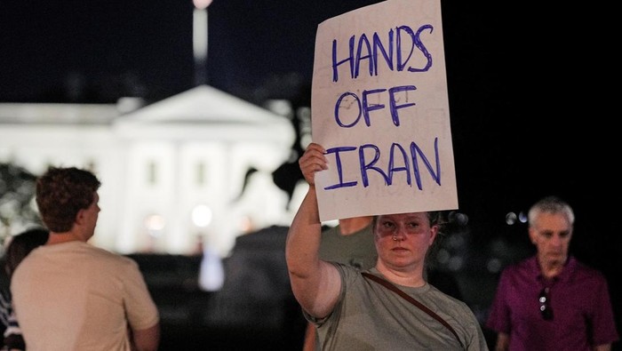 Warga AS Marah Trump Ikutan Perangi Iran Emma Edwards holds a poster while protesting outside Lafayette Park, following U.S. strikes on Iran's nuclear facilities, in Washington, D.C., U.S., June 21, 2025. REUTERS/Ken Cedeno