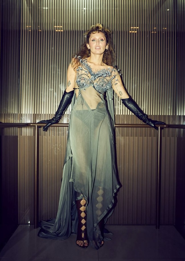Gaunnya menjuntai dari kain super tipis yang dengan jelas menampilkan siluet tubuh penyanyi 31 tahun itu Penampilannya dilengkapi dengan sarung tangan hitam sepanjang siku dan sandal gladiator berwarna cokelat.  Foto: dok. Instagram @mileycyrus