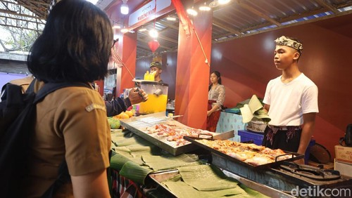 Pedagang ayam panggang memajang daging ayam mentah di atas meja terbuka di area kuliner PKB 2025 di Art Center Denpasar, Senin (23/6/2025). (Aryo Mahendro/detikBali).