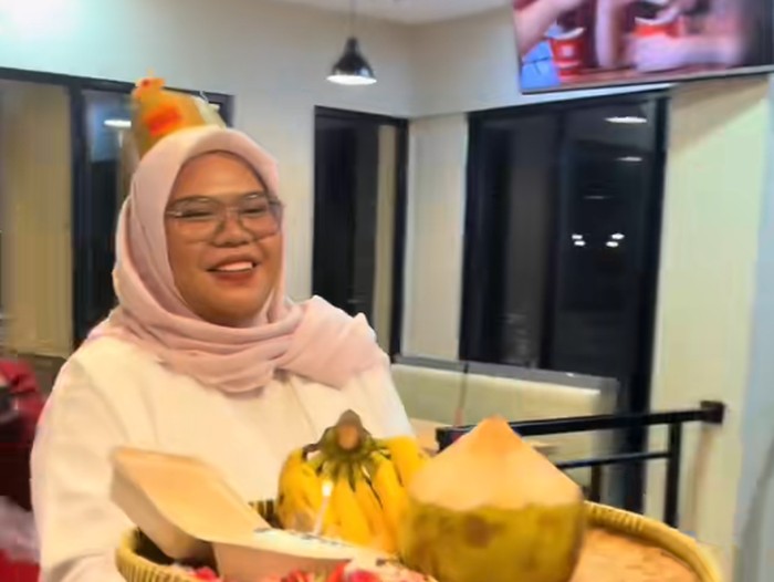 Wanita ini dan teman-temannya memberikan kue dalam bentuk sajen untuk temannya yang sedang berulang tahun.