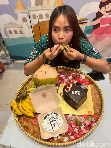 Wanita ini dan teman-temannya memberikan kue dalam bentuk sajen untuk temannya yang sedang berulang tahun.