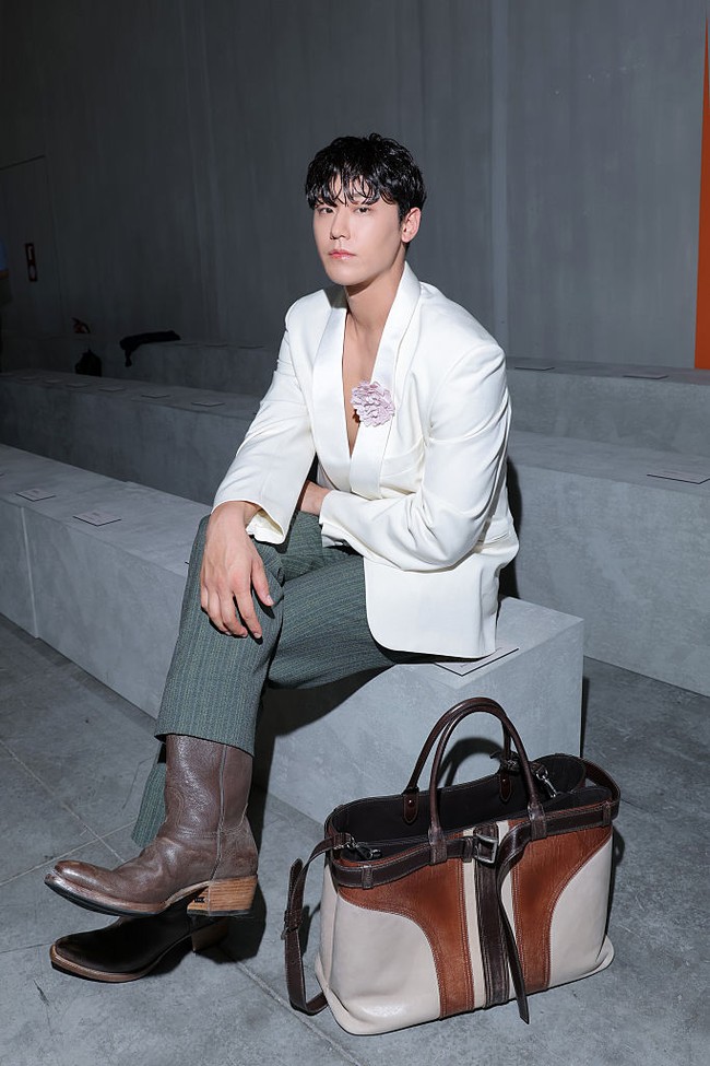 Kekasih Lim Ji Yeon itu memakai blazer putih tanpa dalaman, dengan paduan celana hijau garis-garis dan sepatu boots. Penampilannya dilengkapi dengan koleksi tas Prada dan hiasan bros bunga di dada kirinya. Foto: Getty Images