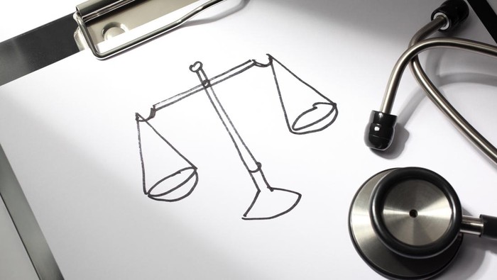 Healthcare concept. Justice scale drawn on a doctors clipboard with stethoscope.