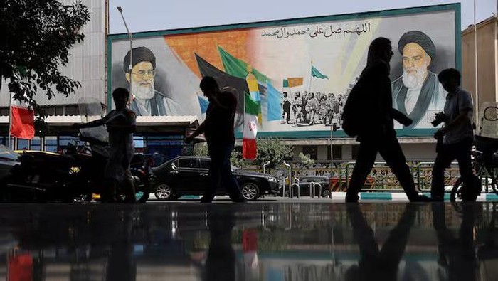 People walk next to a mural with a picture of Irans Supreme Leader, Ayatollah Ali Khamenei, on a street, early hours of ceasefire, in Tehran, Iran, June 24, 2025. Majid Asgaripour/WANA (West Asia News Agency) via REUTERS Purchase Licensing Rights