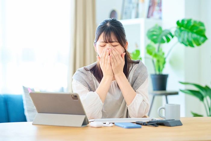 A young woman looking tired while working on a computer in her room