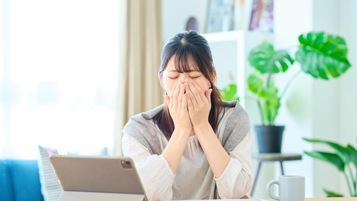 A young woman looking tired while working on a computer in her room