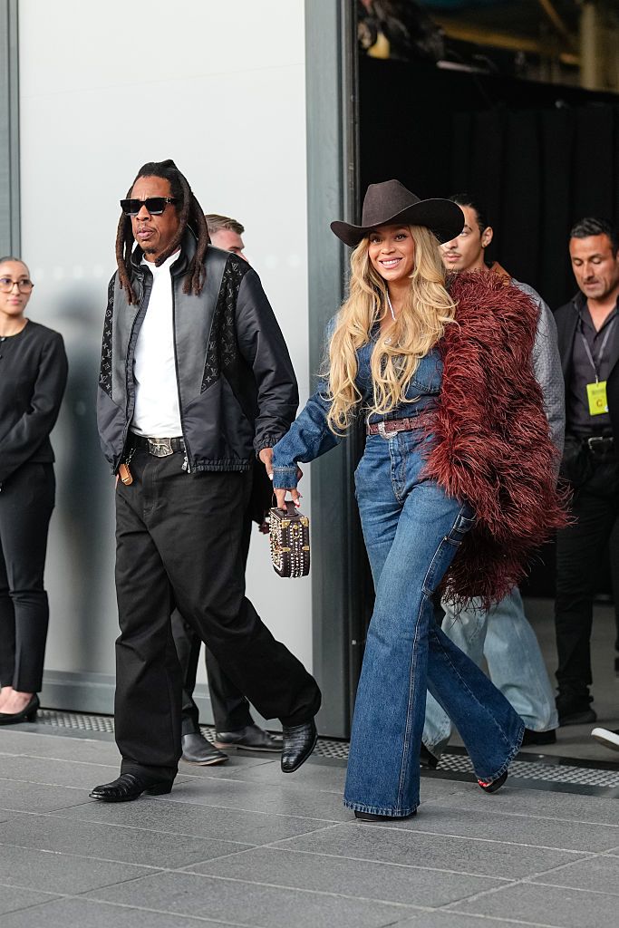 PARIS, FRANCE - JUNE 24: Jay-Z wears a black leather jacket with Louis Vuitton monogram logo print, a white t-shirt, a belt, black wide-leg pants, black leather pointed shoes ; Beyoncé Knowles / Beyonce wears a cowboy hat, a burgundy faux fur fluff coat on one shoulder, a blue denim jacket, blue flared denim pants / jeans, during the Louis Vuitton Menswear Spring/Summer 2026 show as part of Paris Fashion Week on June 24, 2025 in Paris, France. (Photo by Edward Berthelot/Getty Images)