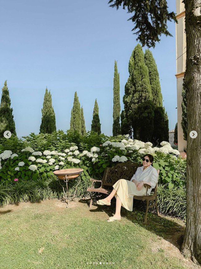 Cantiknya Nagita Slavina berpose memakai rok kuning dan kemeja putih dengan latar belakang taman bunga di Italia. Foto: Dok. Instagram RaffiNagita