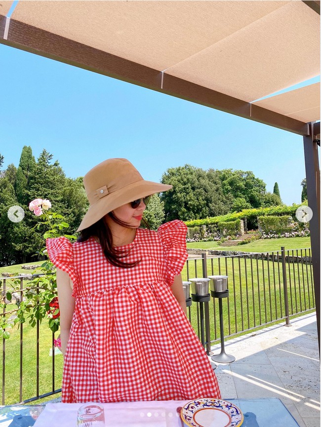 Nagita Slavina menikmati liburannya di Italia dengan berpose di sebuah kafe dengan latar taman bunga yang cantik. Nagita tampil dengan mini dress merah kotak-kotak dari brand asal Denmark, Ganni. Foto: Dok. Instagram RaffiNagita