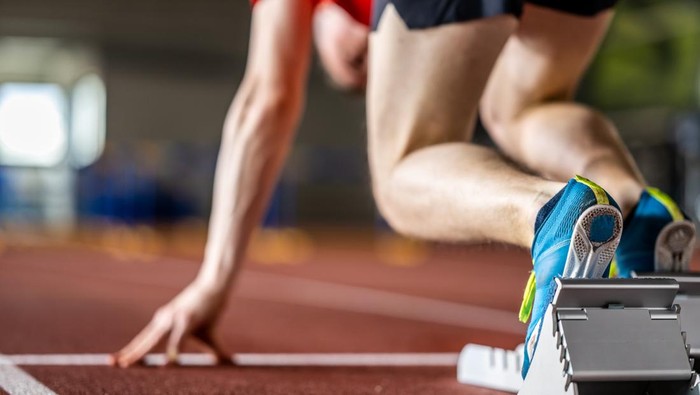 Male athlete legs standing on starting block ready to run at stadium track back view close up