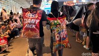 Muda-mudi pengunjung PRJ ini rupanya tak mau ketinggalan tren makanan besar. Ada pria yang menggendong tas dari mie Gaga sementara yang perempuan menggendong camilan Oops. Foto: Tim detikfood