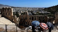 Para turis memegang payung untuk melindungi diri dari terik matahari selama kunjungan mereka ke Teater Dionysus di bukit Acropolis, saat gelombang panas melanda Athena, Yunani, Jumat (27/6). REUTERS/Stelios Misinas
