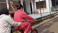 Nagita Slavina yang memakai piyama merah dipegangi karyawan saat belajar naik sepeda. (Foto: dok Instagram raffinagita1717)