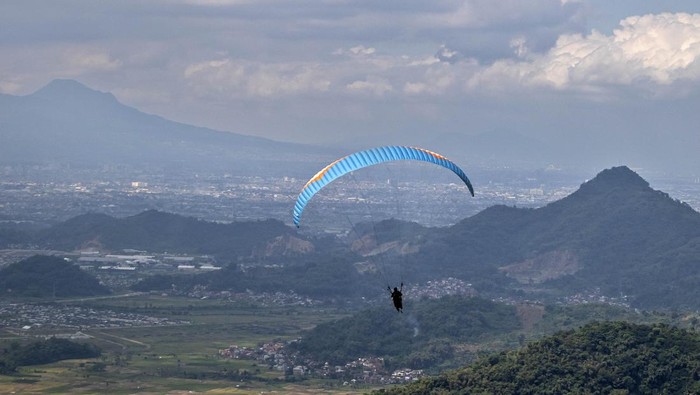 Wisatawan bersama pilot paralayang mengudara di atas kawasan Cihampelas, Kabupaten Bandung Barat, Jawa Barat, Senin (30/6/2025). Pariwisata olahraga (sport tourism) yang dikelola oleh Paralayang Bandung Raya tersebut menawarkan paket wisata paralayang dengan terbang dari ketinggian 1.080 meter di atas permukaan laut (mdpl) sekaligus mengenalkan potensi pariwisata di daerah itu. ANTARA FOTO/Abdan Syakura