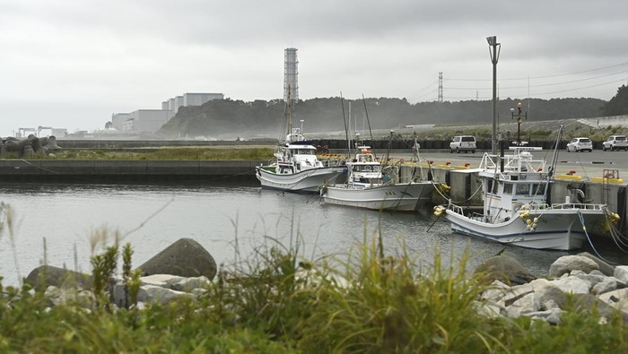 7 Negara Asia yang Punya PLTN, Indonesia Masih Rencana FUKUSHIMA, JAPAN - AUGUST 18: A view of the Fukushima Daiichi nuclear power plant in the background of a fishing port where boats are moored in Okuma City, Fukushima Prefecture, Japan, where radioactive water was discovered leaking from reactor unit 2 on August 18, 2024. Tokyo Electric Power Company (TEPCO), the operator of Japan's Fukushima nuclear power plant, is continuing its controversial program to release 1.34 million tons of